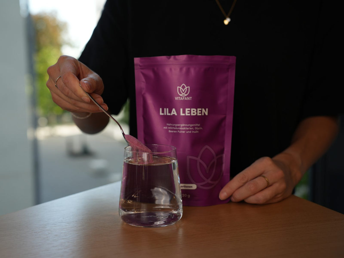 Lila Leben Pulver wird vom Teelöffel in ein Glas Wasser gegeben